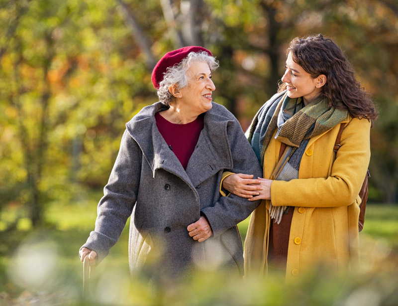 Two women smiling, walking outdoors in autumn.